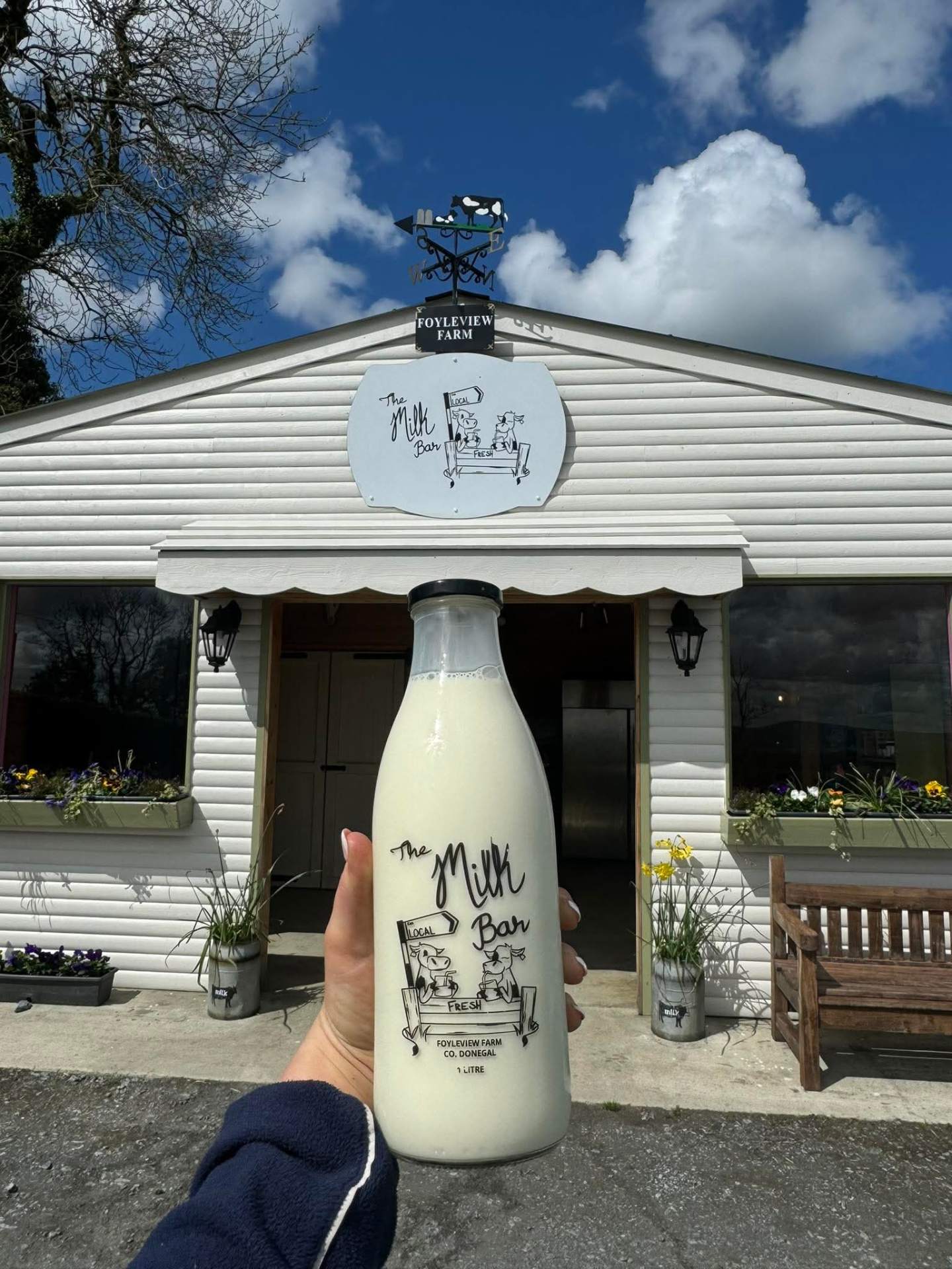 A bottle of The Milk Bar fresh milk held up in front of the Foyleview Farm shop